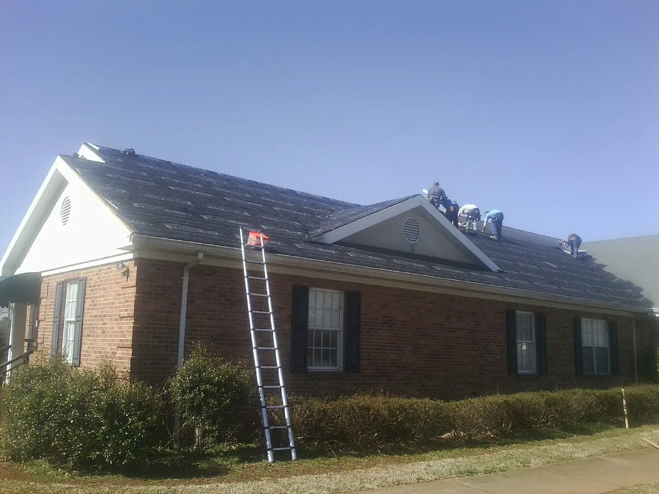 Crew tearing shingles off a brick ranch roof with a ladder set — Metal Roof Repair work by our crew in Atwood
