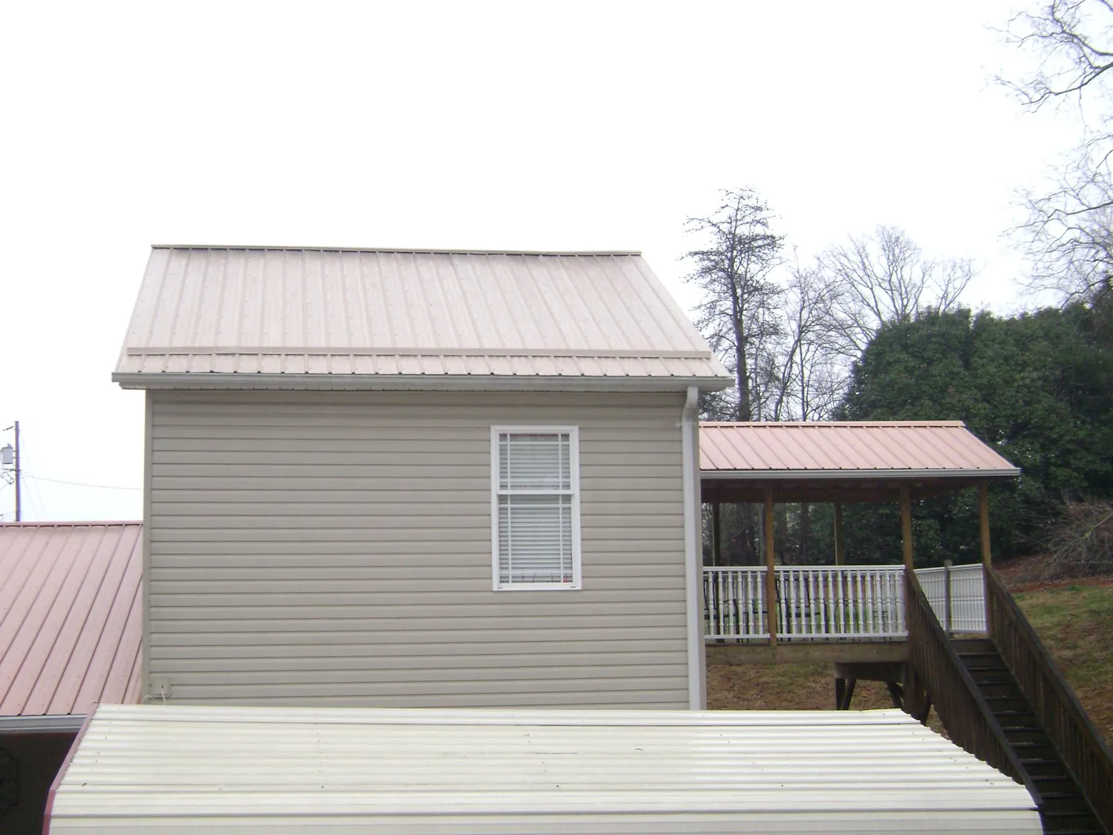 Tan metal roofs on a two story addition and attached porch, from a Roof Replacement job in Atwood